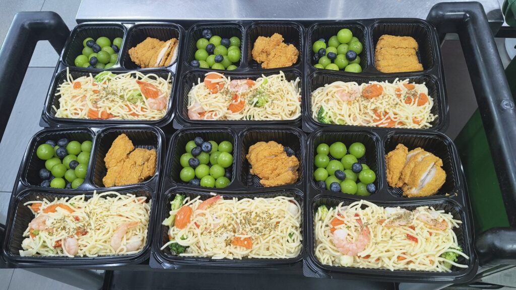 Six bento sets with prawn pasta, fried chicken and fresh fruit, prepared by Catering Corner