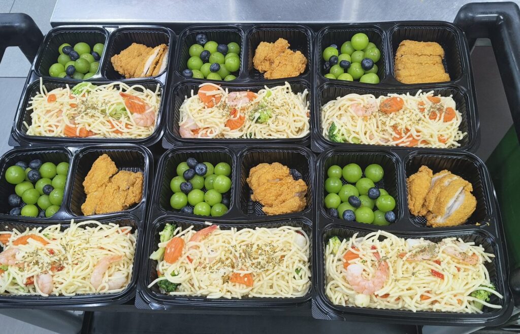 Six bento sets with prawn pasta, fried chicken and fresh fruit, prepared by Catering Corner