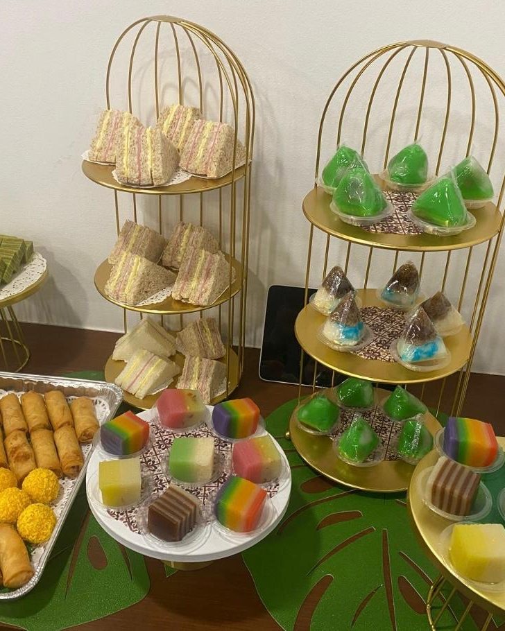 Tea-break spread with sandwiches, kueh lapis, rainbow kueh and spring rolls on gold birdcage stands for a staff event