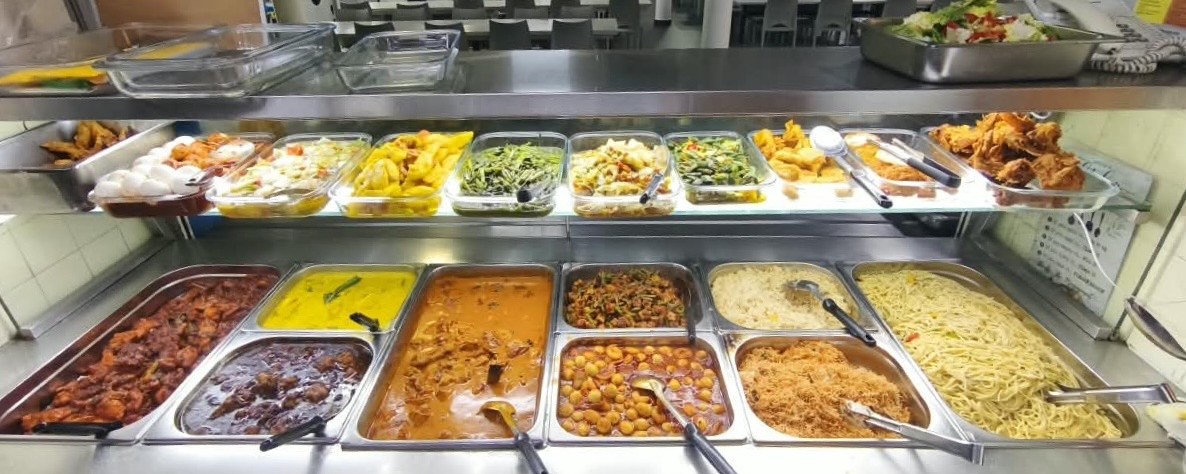 Hot food line at a staff cafeteria with curries, chickpeas, rice and noodles